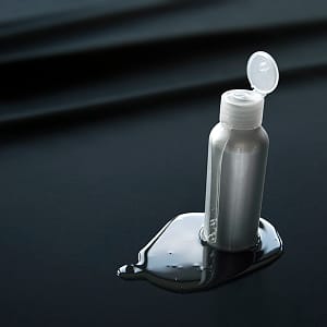 Lubrication - Silver lube bottle with lube running down and pooling on a black Sheets of san francisco fluidproof sheet